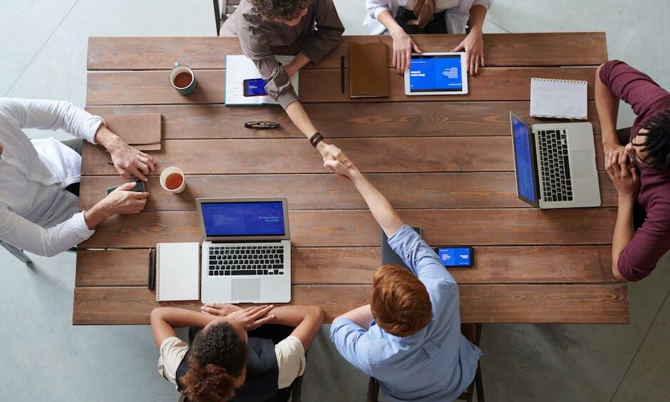 Overhead view of colleagues in a work meeting using laptops and tablets, emphasizing teamwork and technology.