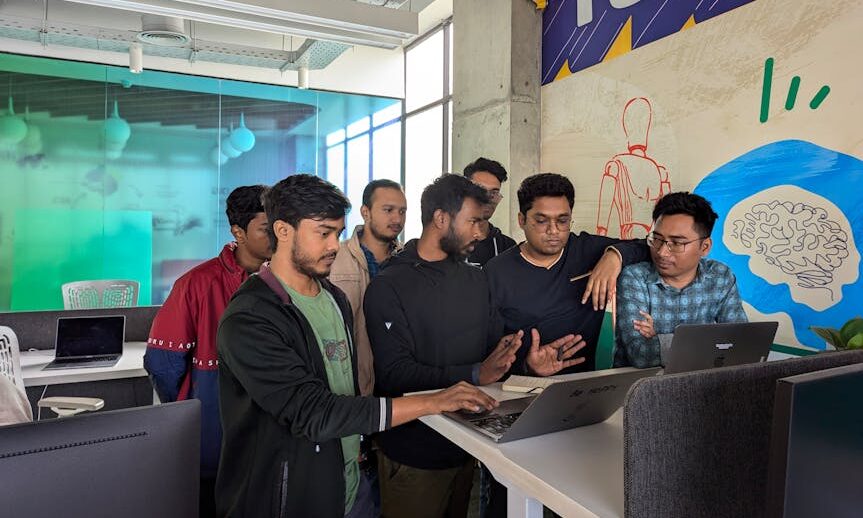 Young professionals collaborate around a laptop in a vibrant, modern office environment.